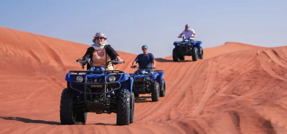 Tourists navigate powerful blue 400cc quad bikes up and down the sloping sand dunes of Dubai's Lahbab Desert, enjoying an exciting off-road adventure.