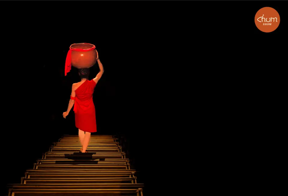 나트랑 Đó 극장 춤 쇼에서 붉은 옷을 입은 공연자가 머리에 항아리를 이고 계단을 오르며 생명과 연결을 상징하는 엄숙한 의식을 표현합니다.