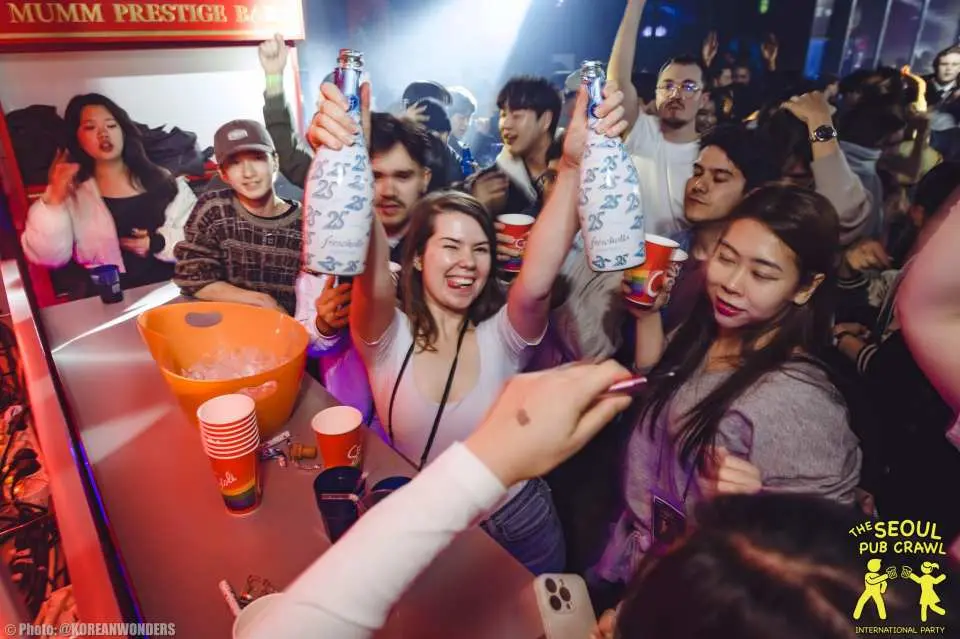 Du khách tham gia chuyến khám phá quán bar Seoul nâng chai và ly đồ uống trong câu lạc bộ đêm sôi động để ăn mừng.