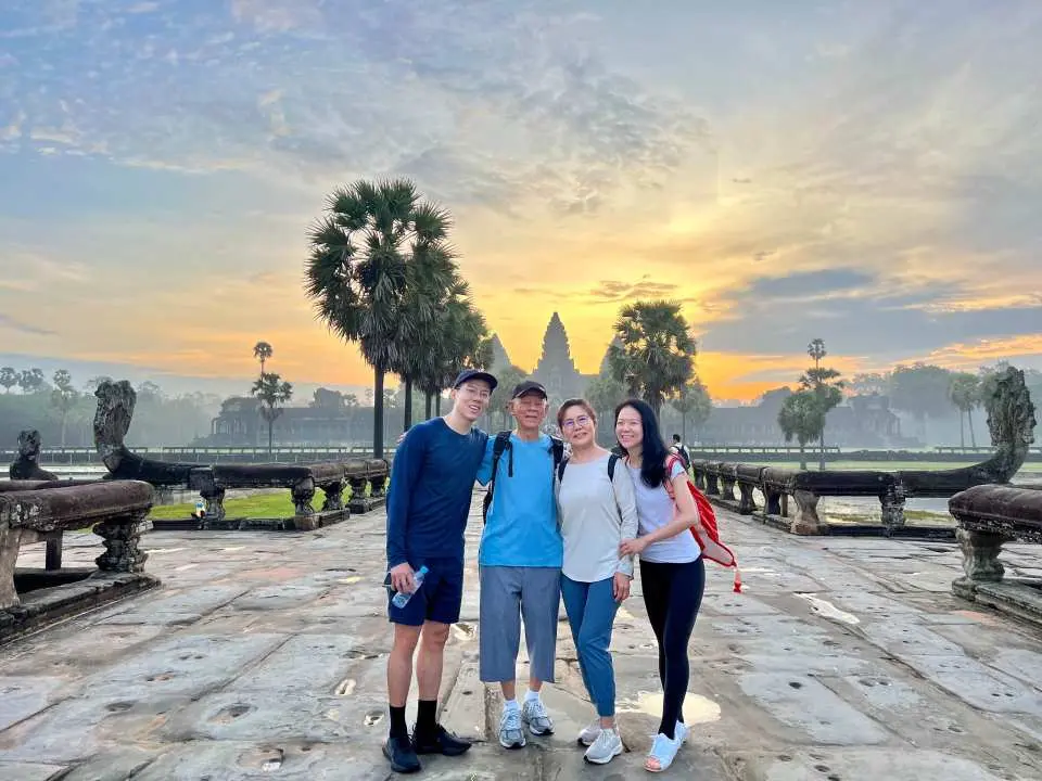 A joyful group of four travelers poses in front of the magnificent Angkor Wat temple, silhouetted against a vibrant sunrise, capturing a perfect tour moment.