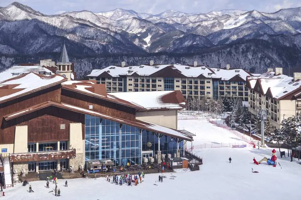 Grand resort buildings at High1 Ski Resort are nestled beside snowy slopes, backed by majestic snow-capped mountains, offering premium skiing, accommodation, and resort facilities.