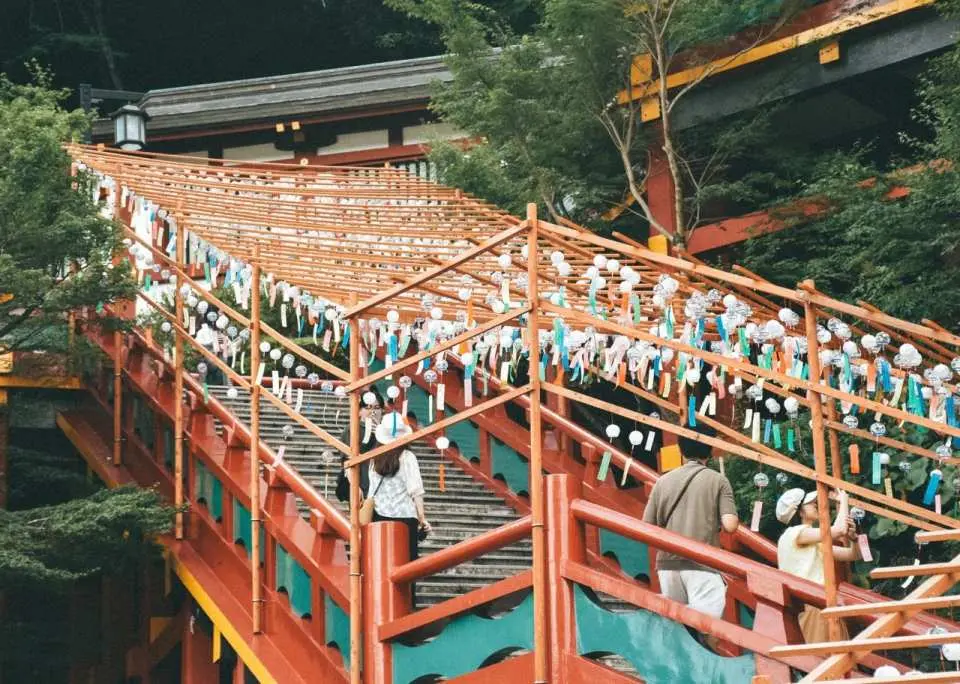 九州佐賀祐德稻荷神社的鮮豔紅橋與階梯，掛滿祈福繪馬或風鈴，信徒與遊客正拾級而上，體驗神聖氛圍。