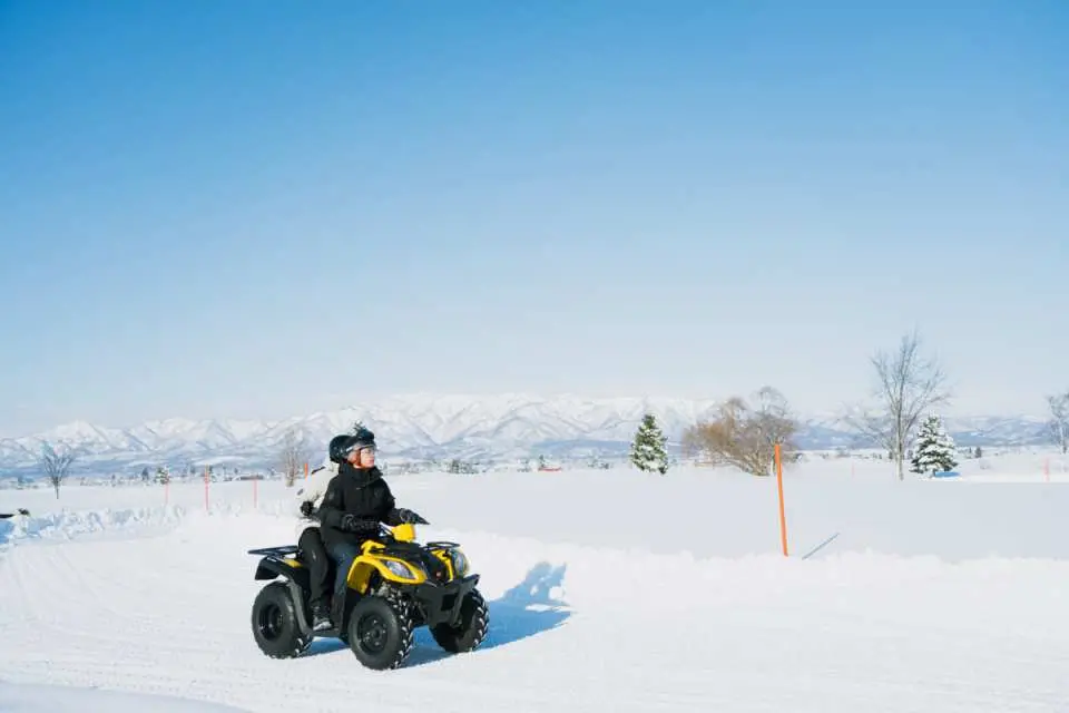 喺美唄雪上樂園，遊客駕駛黃色四驅越野車喺廣闊雪地上奔馳，體驗北海道冬季獨特嘅雪地冒險同速度快感。