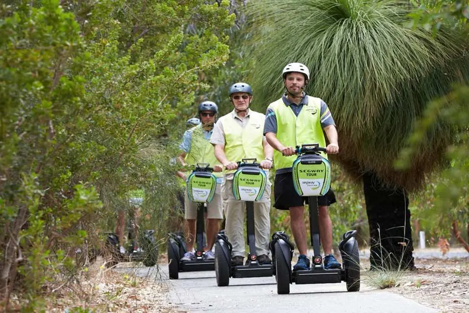 Participants wearing helmets and high-visibility vests explore the natural landscape along a tree-lined path during a King's Park Segway tour in Perth.
