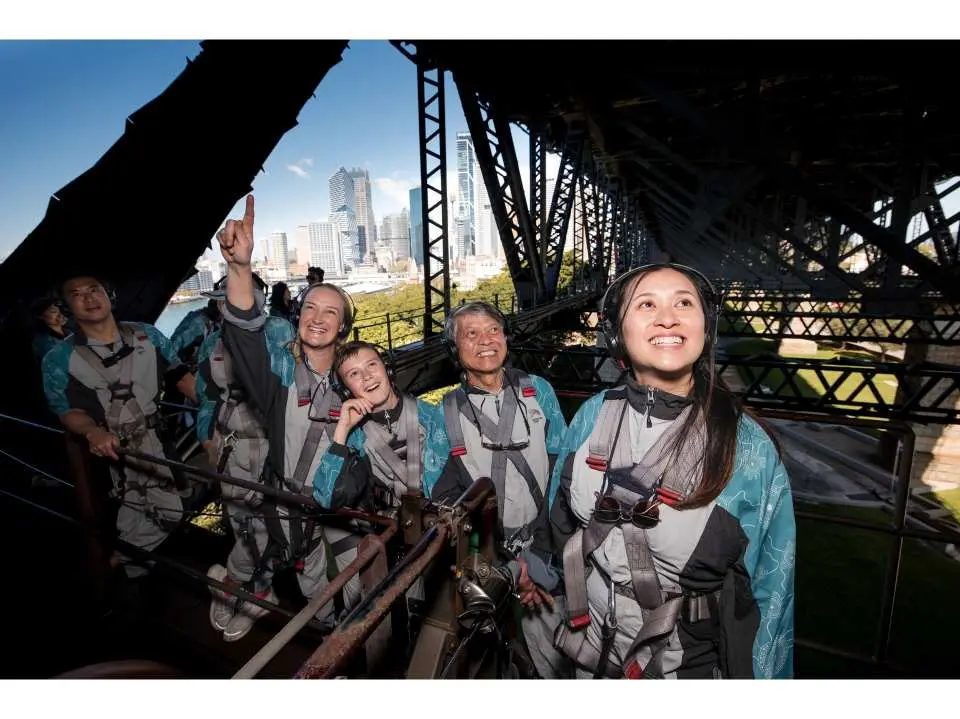 Tourists marveling at the expansive Sydney city and harbour views through the steel framework of the Sydney Harbour Bridge's lower structure during the guided tour.