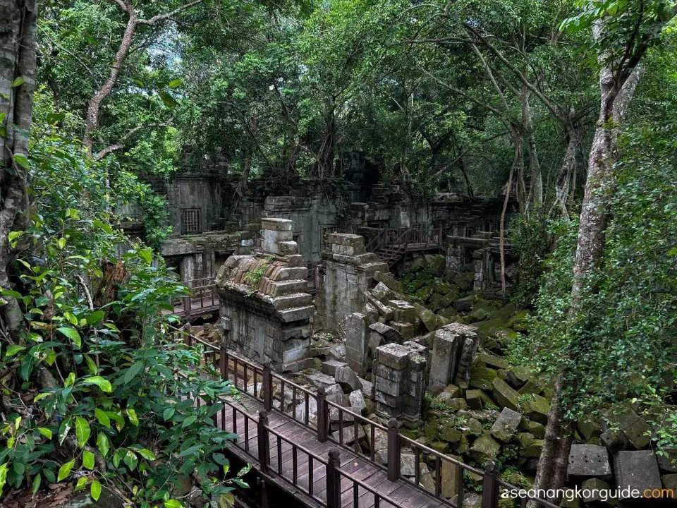 Exploring the atmospheric jungle-covered ruins of Beng Mealea temple in Cambodia, with wooden walkways guiding visitors through the ancient collapsed structures.