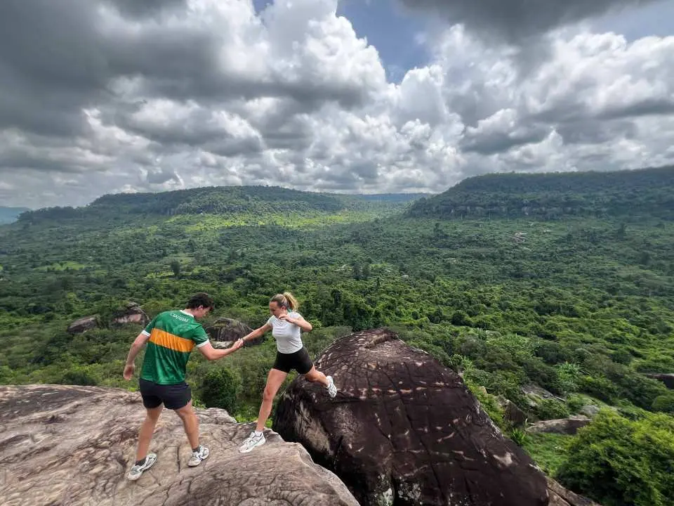 Couple enjoying the breathtaking panoramic views of the lush green landscapes and rolling hills from a rocky outcrop on Phnom Kulen, Cambodia.