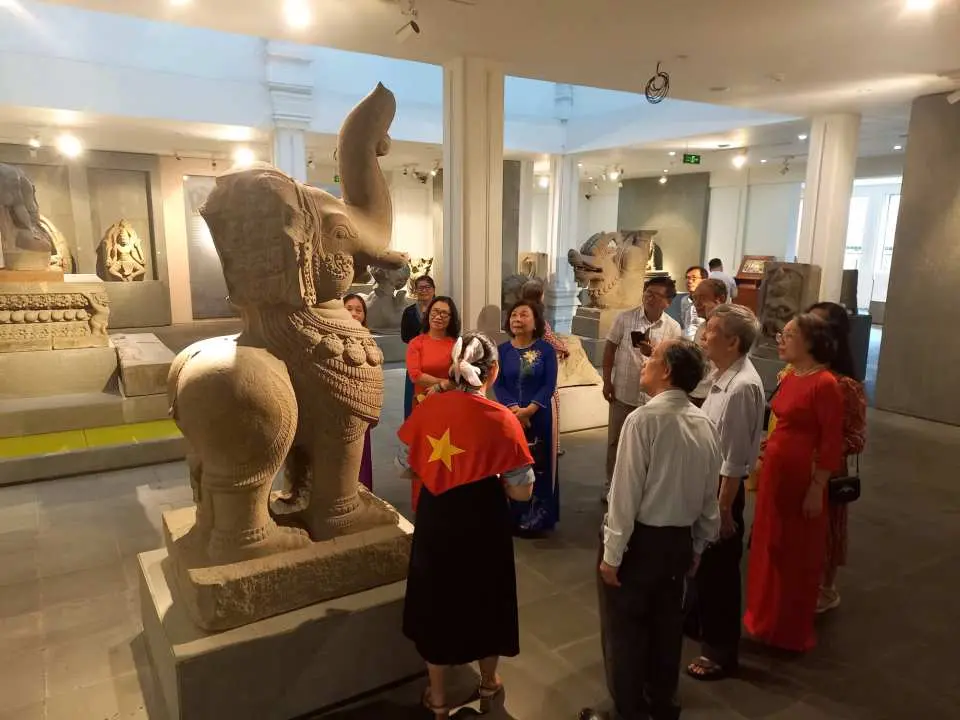 峴港佔婆博物館內，導遊正向一群遊客介紹大型神獸石雕，展現互動式語音導覽體驗，讓訪客深入了解佔婆王國的歷史文化。