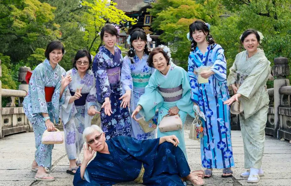 Group of women in colorful yukatas posing cheerfully on a bridge in Kyoto Arashiyama, capturing joyful friends or family moments with a professional travel photographer.