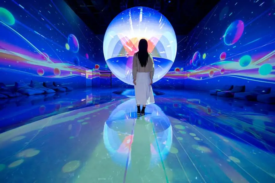 韓國仁川Le Space沉浸式媒體藝術展中，一名遊客站在藍色與紫色宇宙光影環繞的空間，前方是巨大的發光球體，營造出深邃的太空奇幻感。