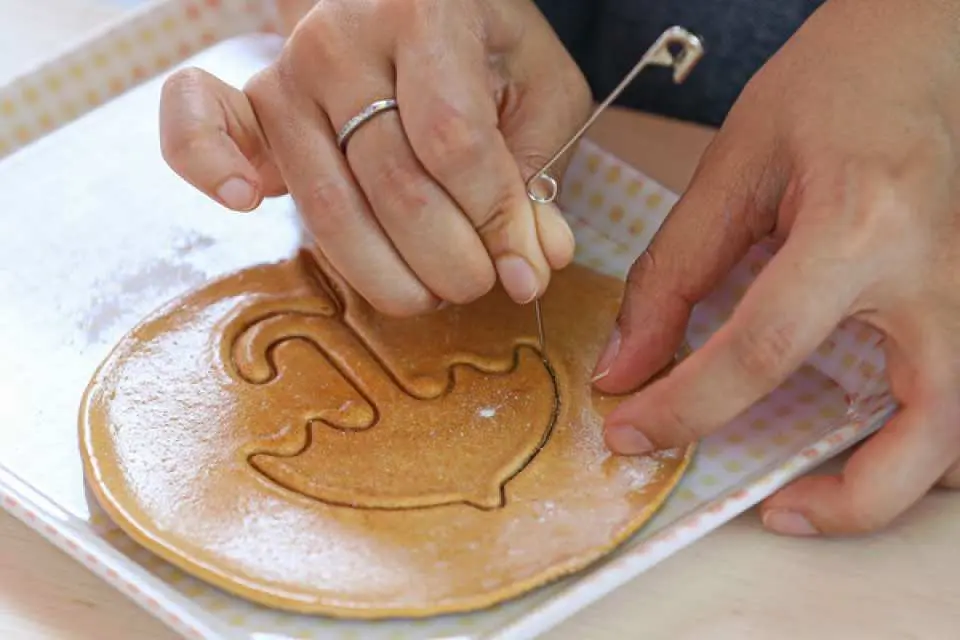 一双手正用针小心翼翼地在韩国椪糖上压出图案，这是经典的韩剧互动游戏，增加野餐乐趣。