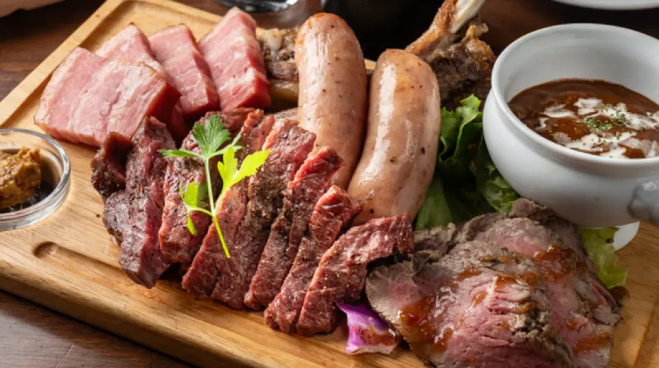 我们的招牌菜「烤箱烤肉拼盘」汇集了各种肉类，让您尽享美味，包括鲜嫩多汁的大香肠、厚切培根、排骨、自制烤牛肉和半腌制牛筋。这道烤肉拼盘在烤箱中慢烤，大约需要20分钟即可完成。此外，我们还提供多种精选牛排，包括风味浓郁的瘦肉和鲜嫩多汁的西冷牛排。