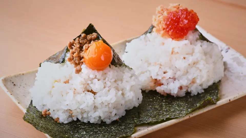 我们提供份量十足的大饭团，每个饭团都馅料丰富。下单后，我们会精心制作，并在您面前现场呈上。由于海苔只包裹了一面，入口时能感受到酥脆的口感。随后，米饭软糯地融化，带来令人愉悦的味觉体验。我们对食材也精挑细选，选用有明产的海苔和南鱼沼产的越光米。我们精心挑选了超过20种食材，为您带来丰富的味觉体验。请品尝这道由专业厨师监督制作的美味佳肴。