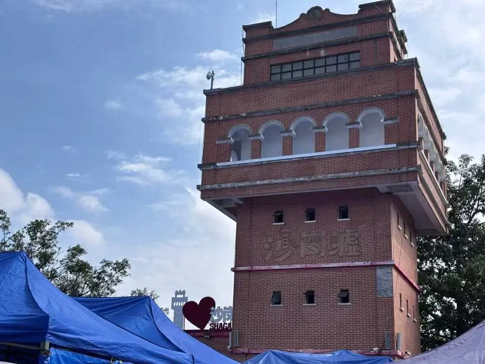 中山【沙崗墟】旁的歷史建築，紅磚外牆風格獨特，與前景的市集藍色帳篷形成對比，展現百年市集風貌。