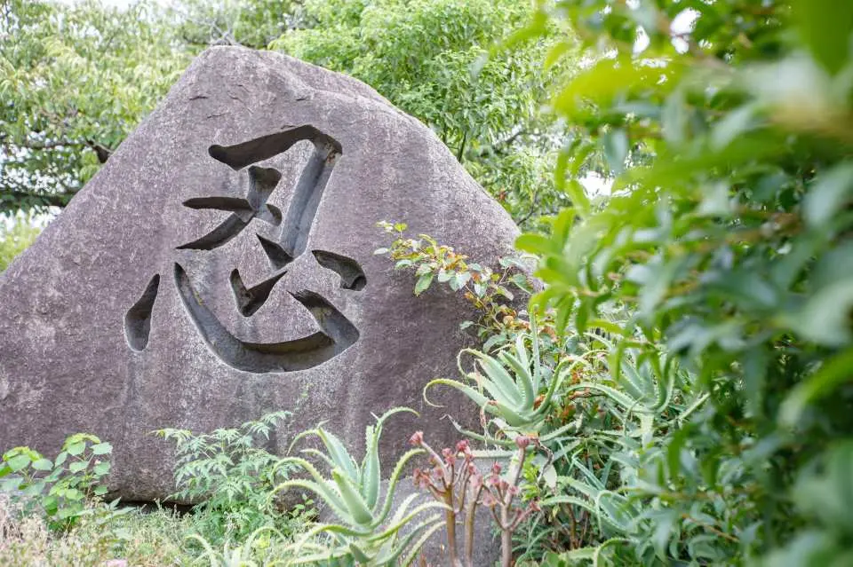 Cận cảnh tảng đá lớn khắc chữ "忍" (nin) trong Công viên Oohama Osaka, tượng trưng cho tinh thần sumo giữa cây xanh tươi tốt.