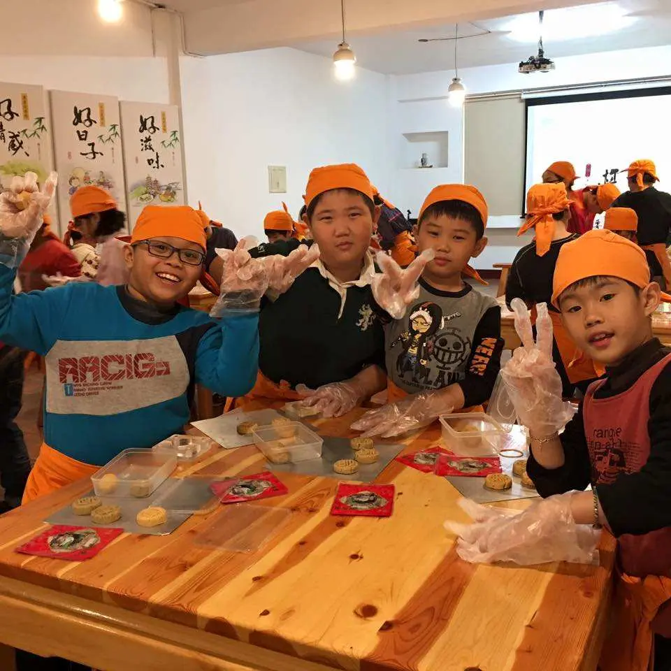 高雄中外餅舖棋餅文創館內，一群戴著橙色帽嘅小朋友正開心參與棋餅DIY體驗，親手製作象棋造型糕點，展現全國創意類第一名嘅趣味親子活動。