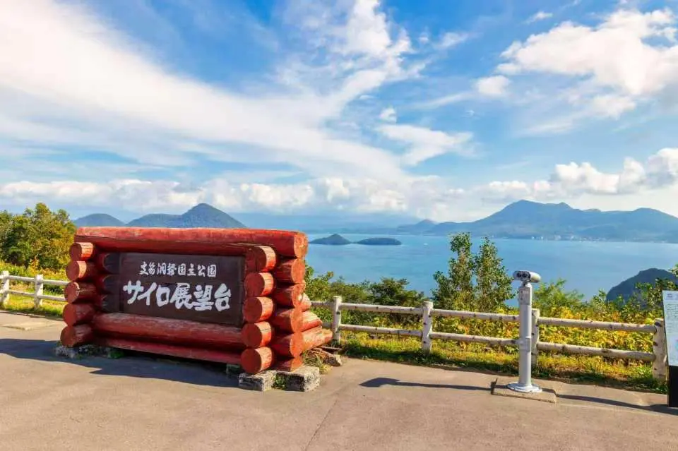 站在著名的「支笏洞爺國立公園 筒倉展望台」木製地標前，將整座洞爺湖的平靜水面與湖心島盡收眼底。天氣晴朗時，遠方的山巒如水墨畫般層層疊疊，是來到洞爺湖不能錯過的經典打卡機位！