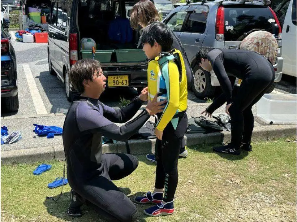 集合・受付。申込用紙を記入後、海へ行く準備を始めます♪ウエットスーツ・マリンシューズ・ライフジャケットなどを装着していきます。しっかりサイズが合っているか確認調整します。