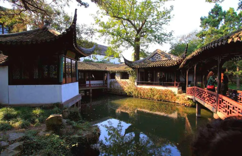 蘇州拙政園的古典園林景色，池塘映照著古色古香的亭閣與廊橋，綠樹環繞，展現江南水鄉獨有的雅致。