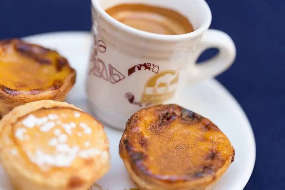 Two tempting Portuguese custard tarts served with aromatic coffee, showcasing the perfect afternoon tea moment for tasting authentic local pastries on the Lisbon walking tour.
