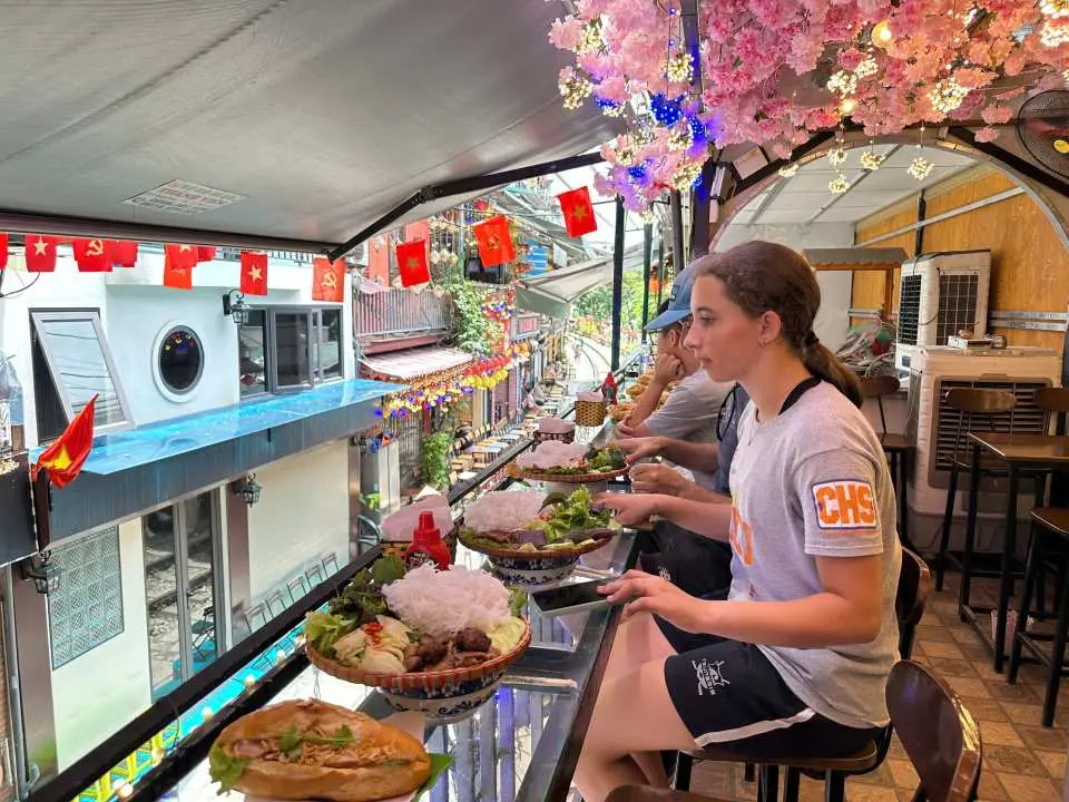 遊客在河內特色街景餐廳，於櫻花裝飾下享用當地美食，俯瞰熱鬧街道，感受越南獨特的用餐氛圍。