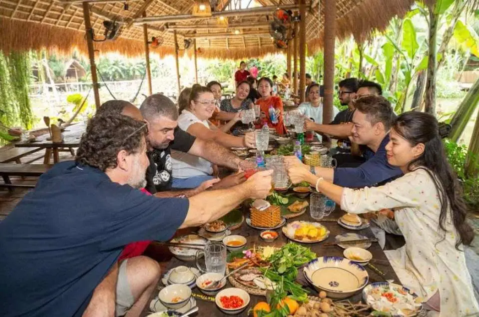 参与芽庄烹饪课的国际游客们，在茅草屋顶下的大长桌旁举杯欢庆，共享亲手制作的丰盛越南美食。