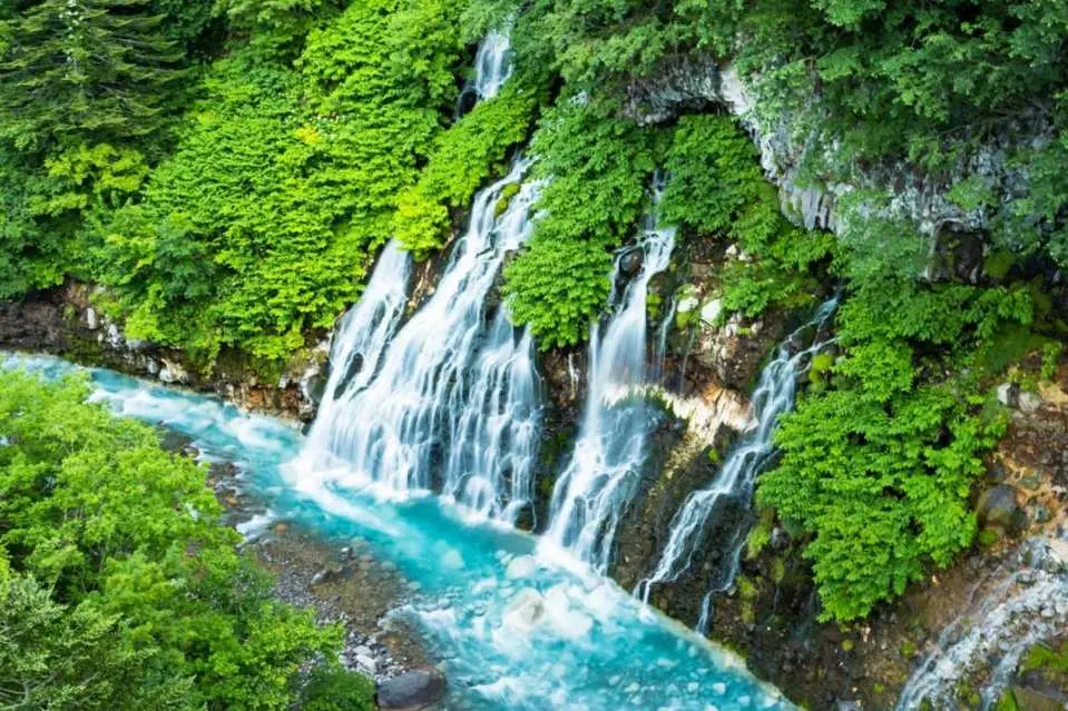 夏日的白鬚瀑布在翠綠山林間傾瀉而下，清澈湛藍的溪流與沁涼水氣交織，宛如北海道秘境中的天然畫卷。