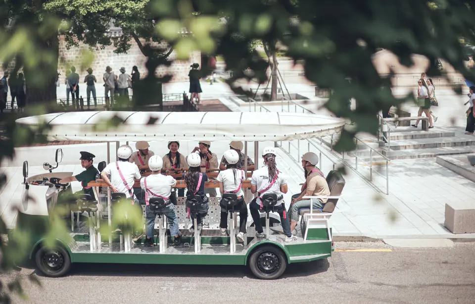 นักท่องเที่ยวบนรถรางปั่นโซลกำลังชื่นชมใบไม้เปลี่ยนสีสีทองและทัศนียภาพเมืองที่ทันสมัยไปตลอดเส้นทาง สัมผัสความงามของฤดูกาลที่เปลี่ยนแปลง