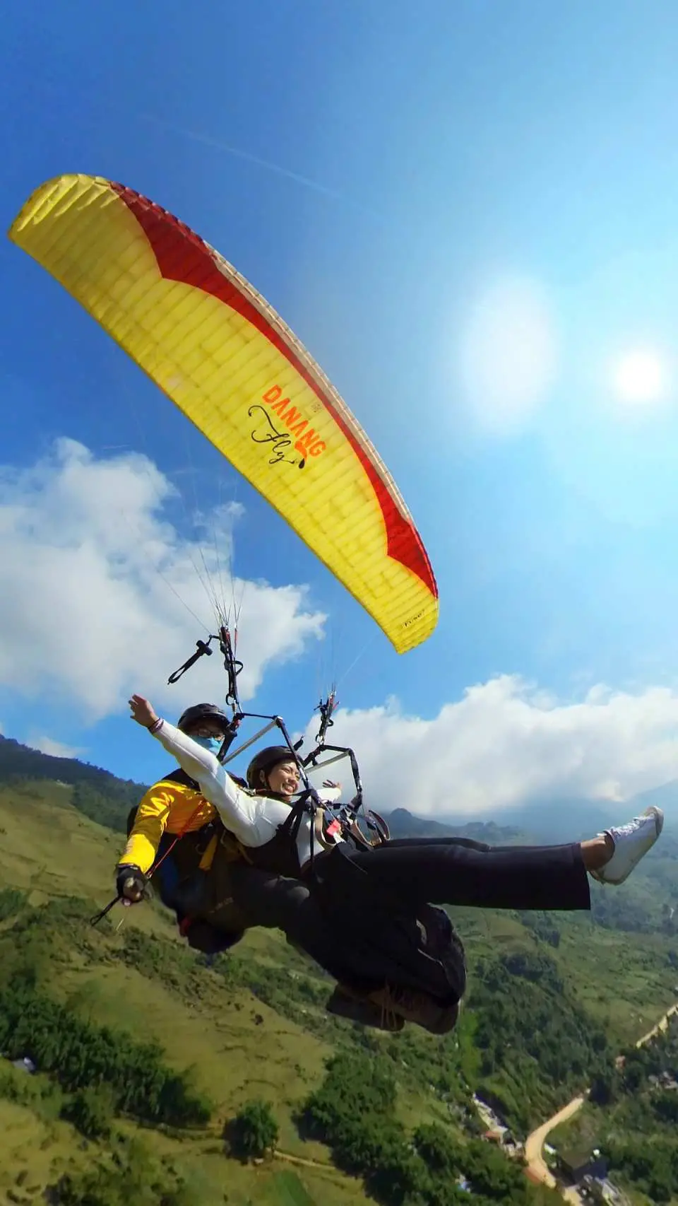 一名乘客乘坐鮮黃色滑翔傘，在晴朗藍天下高高飛翔於沙壩雄偉的綠色山脈和山谷上方，陽光普照。