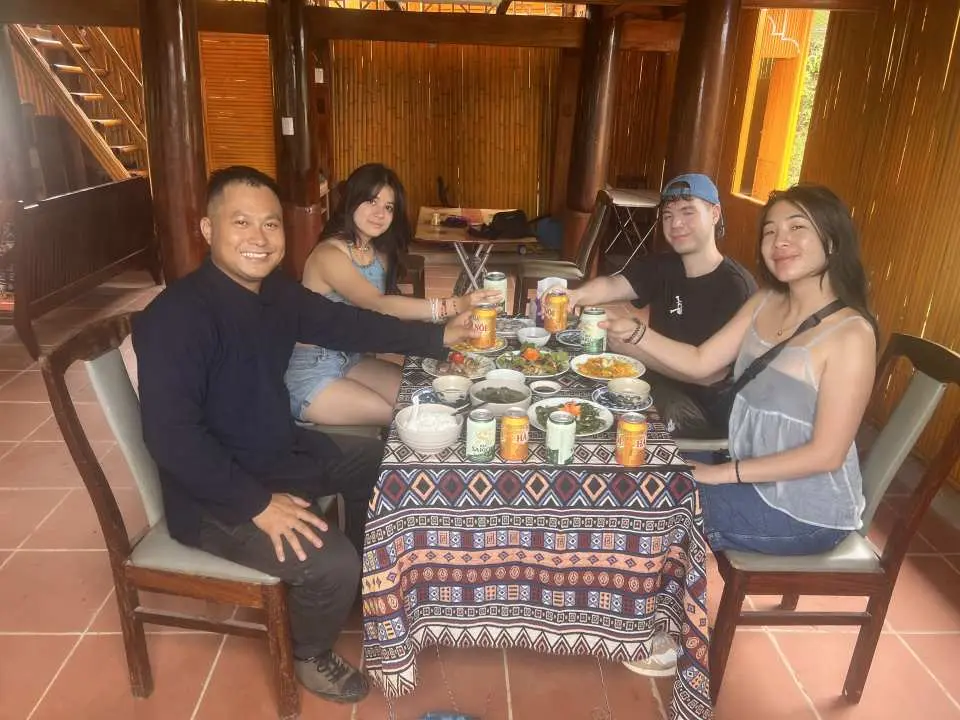 A group of friends toasting with drinks and enjoying authentic Vietnamese cuisine around a table in a traditional homestay, experiencing local life and delicious dinner.