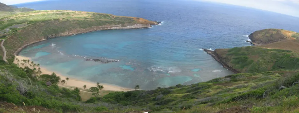 오아후의 초승달 모양 하나우마 베이 자연보호구역의 파노라마 전경. 맑고 푸른 바다, 산호초, 울창한 주변 언덕이 드러납니다.