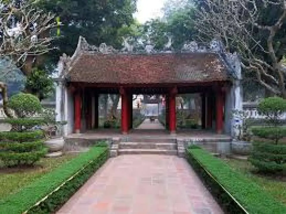 The classical garden entrance of Hanoi's Temple of Literature and Imperial Academy, where a rustic traditional gatehouse nestled in lush greenery leads visitors into the historical halls of Vietnam's first university.