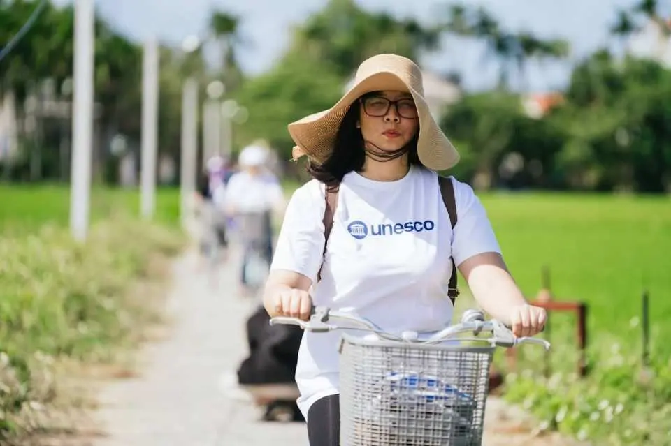 Tourist in a hat cycling through Hoi An countryside path, enjoying the serene rural landscape and eco-tour.