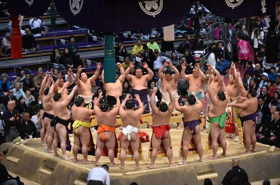 「土俵入り」
大相撲の取組前に行われる、十両・幕内力士が彩り豊かな化粧廻しを締めて土俵に上がる儀式です。観客への紹介や、神事として場の邪気を払う意味合いも持ちます。力士は東西に分かれて登場し、番付の低い順に土俵に上がり、円形に並んで化粧廻しの端をつまんで持ち上げる、軽く手を合わせるなどの所定の動作をします。