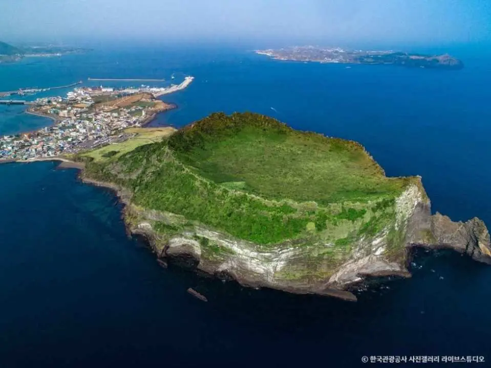 【城山日出峰】是濟州島最具代表性的世界自然遺產，約五千年前由海底火山噴發形成，擁有極高的地質價值。山頂圓形火山口直徑約 600 公尺，環繞如皇冠般的岩石景觀十分壯觀。沿步道登頂，可俯瞰火山與海洋交會的壯麗全景，是感受濟州火山地貌的經典地標。