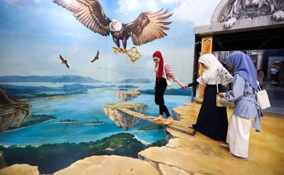 Visitors posing on a wooden plank hanging over a cliff in the 3D Art Museum, Langkawi, Malaysia